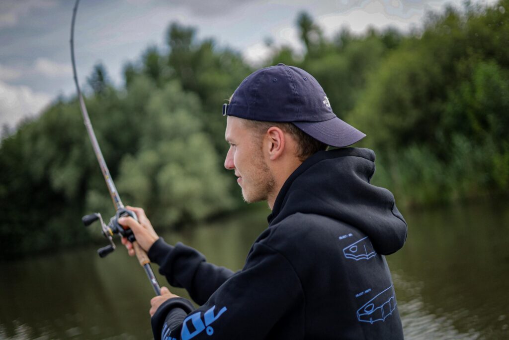 Ein Angler wirft seine Angelrute aus, im Hintergrund ist dichtes Grün zu sehen.